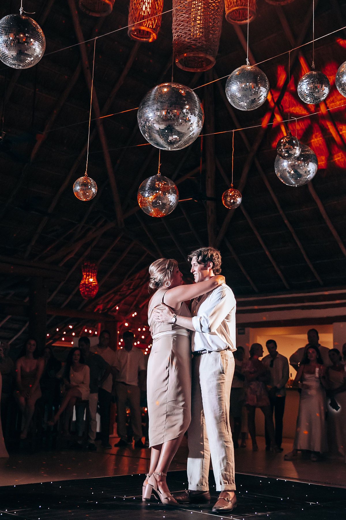 Couple dances beneath dramatic lighting with disco balls and copper lanterns overhead.