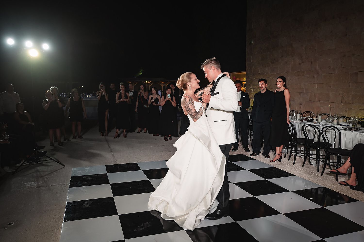 Wedding couple performs romantic dance moves on black and white checkered floor.