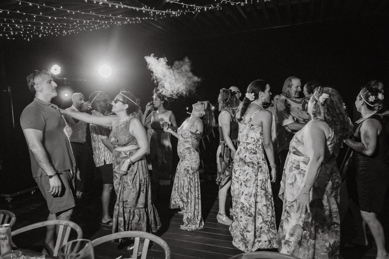 Black and white photo of guests dancing outdoors at a night wedding reception under string lights.