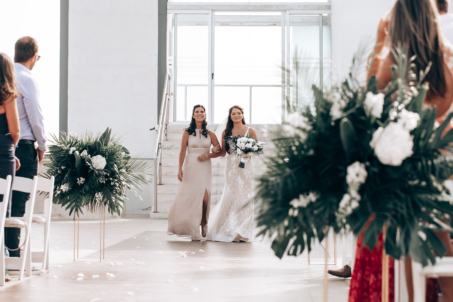 Wedding ceremony space decorated with tropical greenery and white accents.