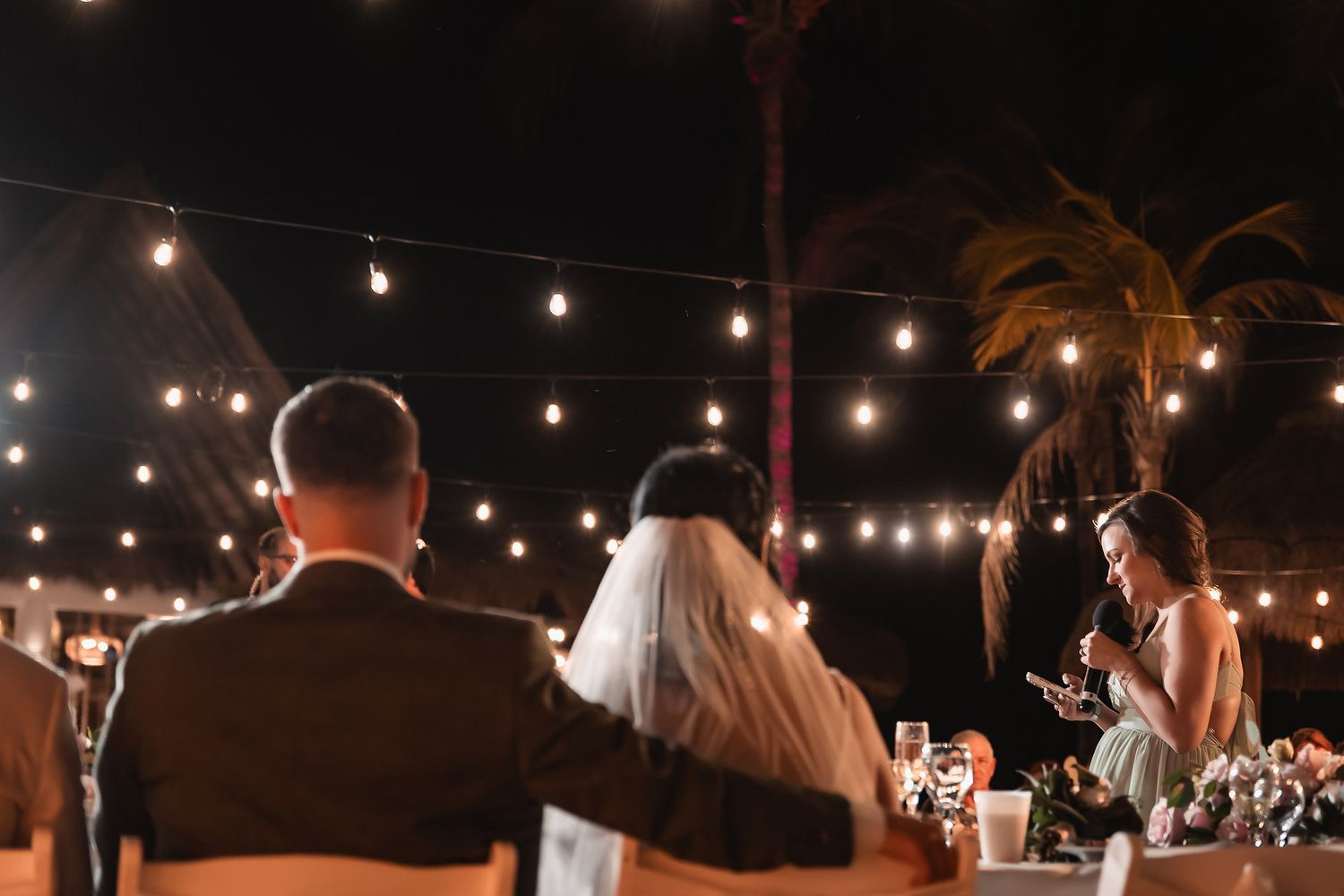 Newlyweds celebrate under romantic string lights at an outdoor evening reception.
