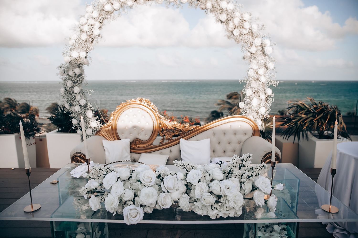 White floral wedding arch and decor setup overlooking the ocean at a beachfront ceremony.