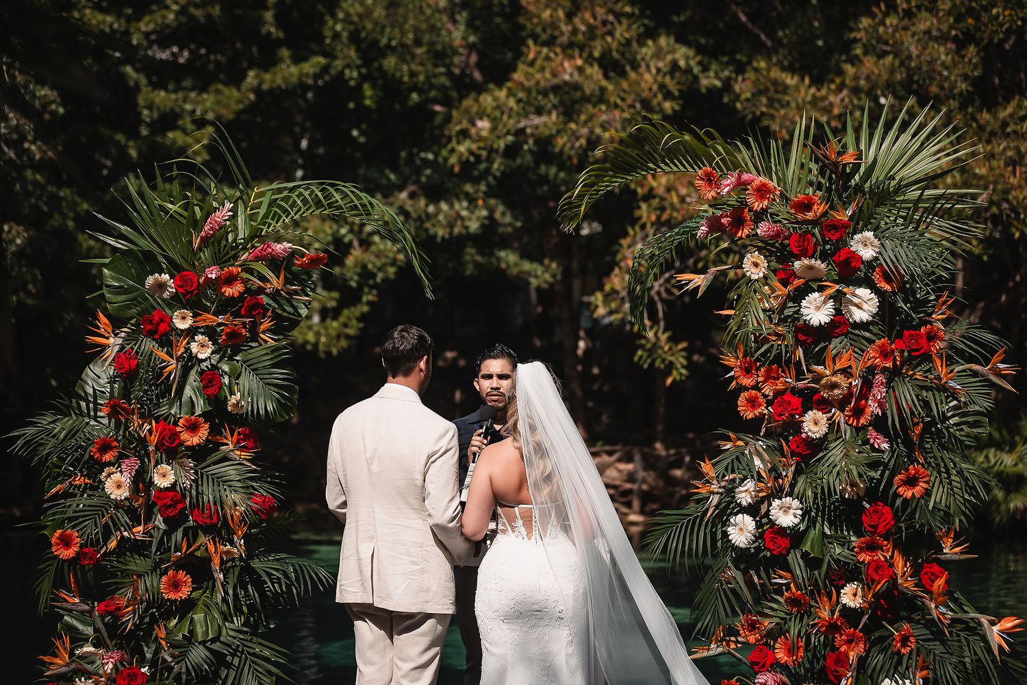 Garden wedding ceremony site with luxurious red floral arrangements and tropical greenery.