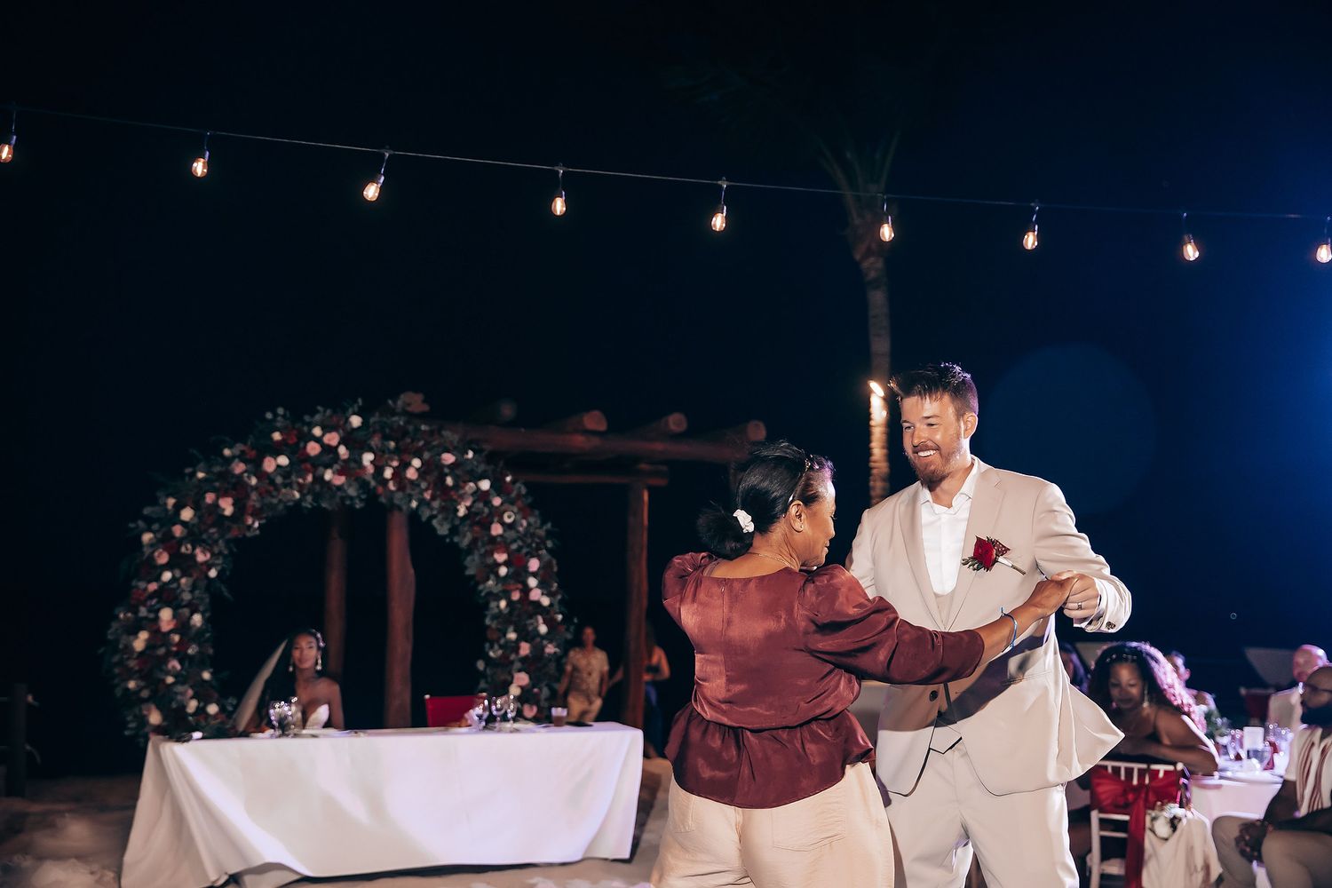 Evening wedding reception with string lights and burgundy decor details.
