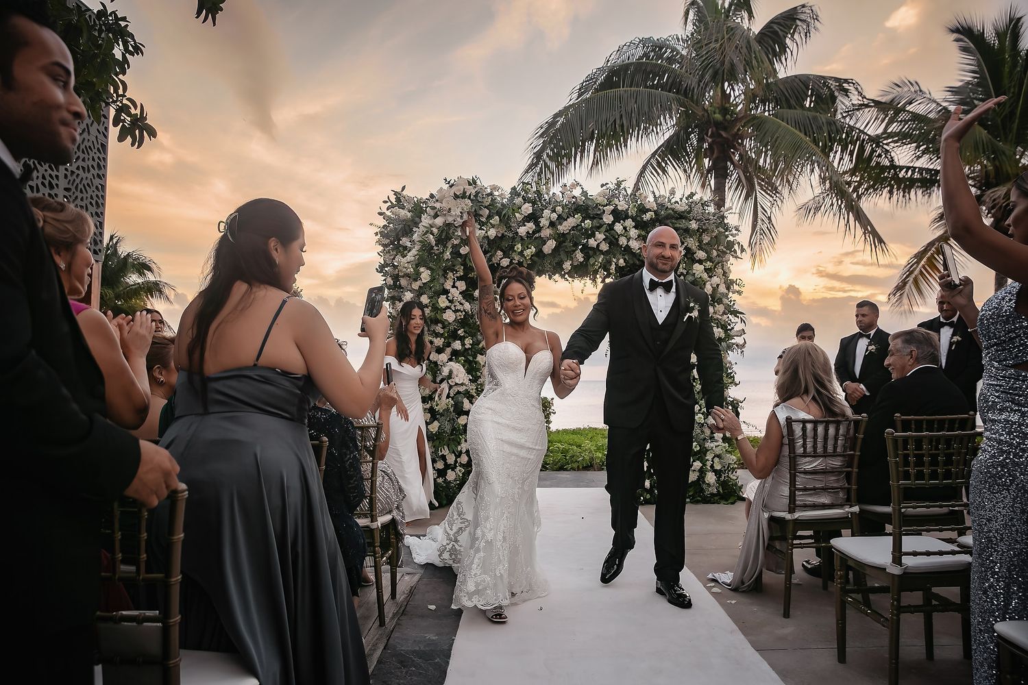 Sunset beach wedding ceremony with palm trees and elegant decor.