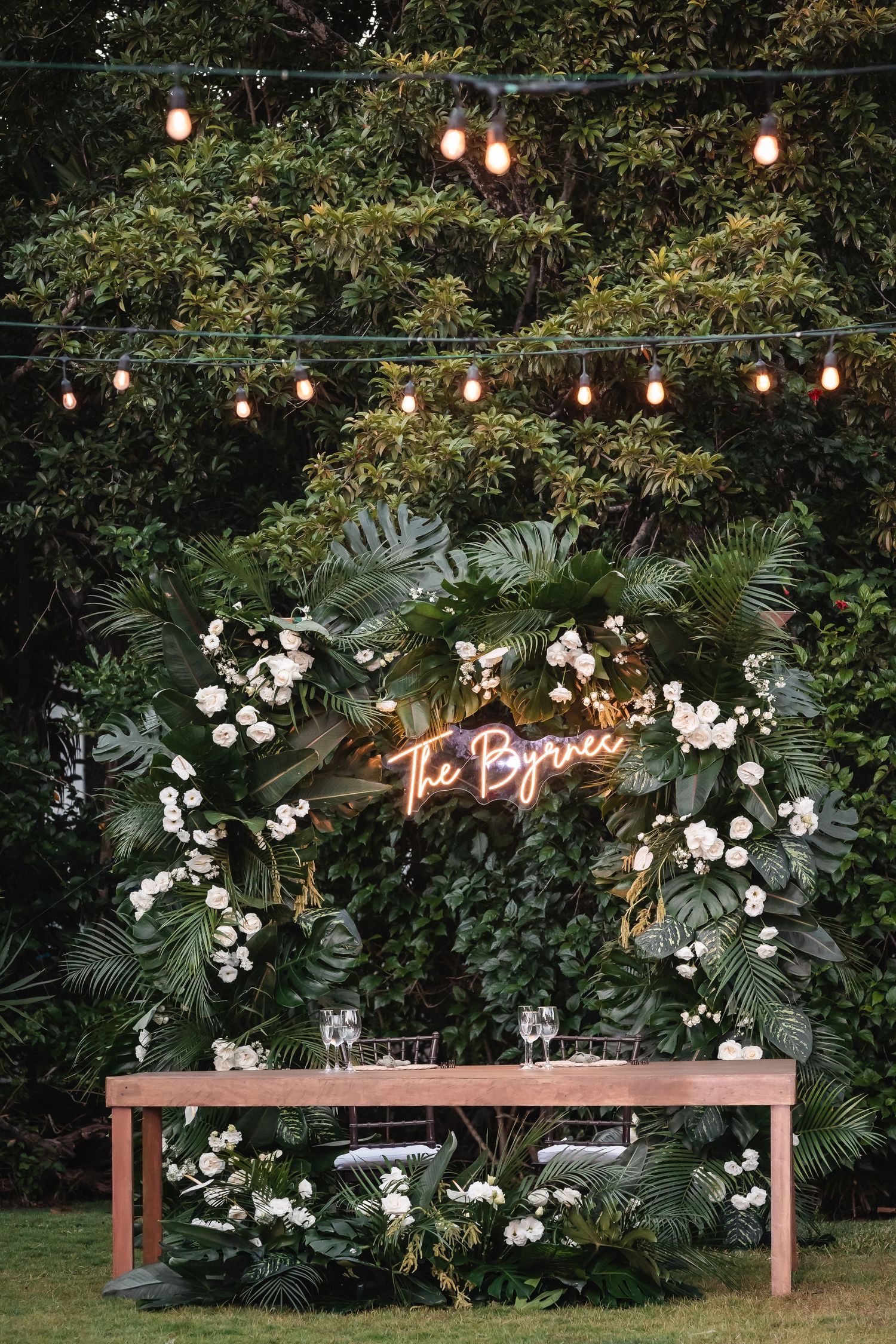 Wedding reception area with illuminated signage, tropical greenery and string lights.