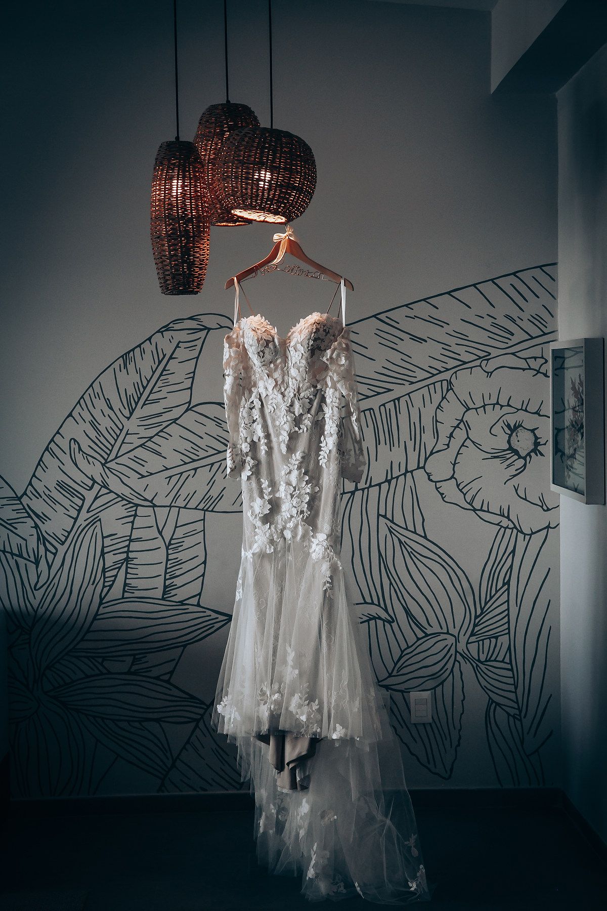 Wedding dress hanging against wall with artistic line drawing mural and pendant lighting.