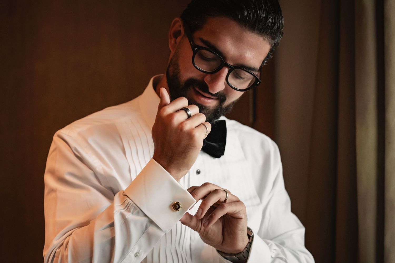 A groom in a crisp white shirt and bow tie adjusts his cufflinks before the ceremony.
