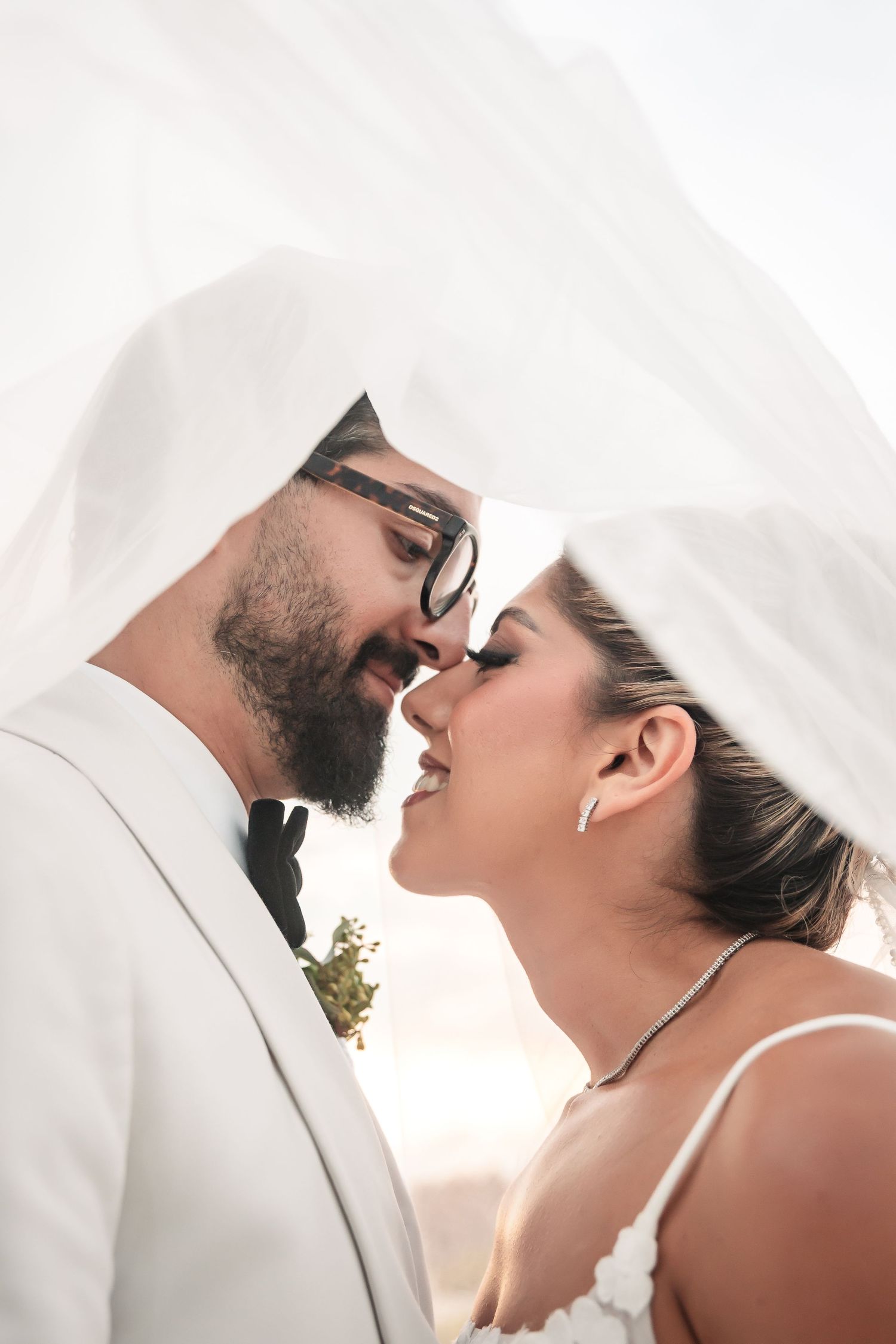 Intimate wedding portrait under flowing white veil during golden hour.