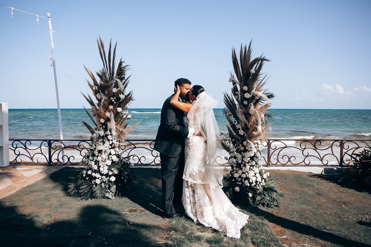 Seaside wedding ceremony setup with decorative floral arrangements against turquoise waters.