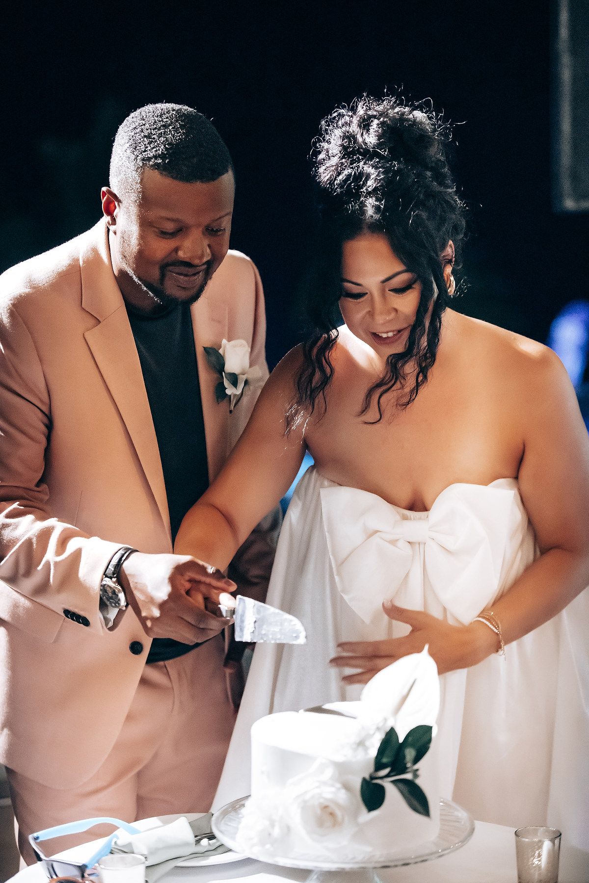 A couple in peach and white attire cut their wedding cake together during an intimate reception moment.