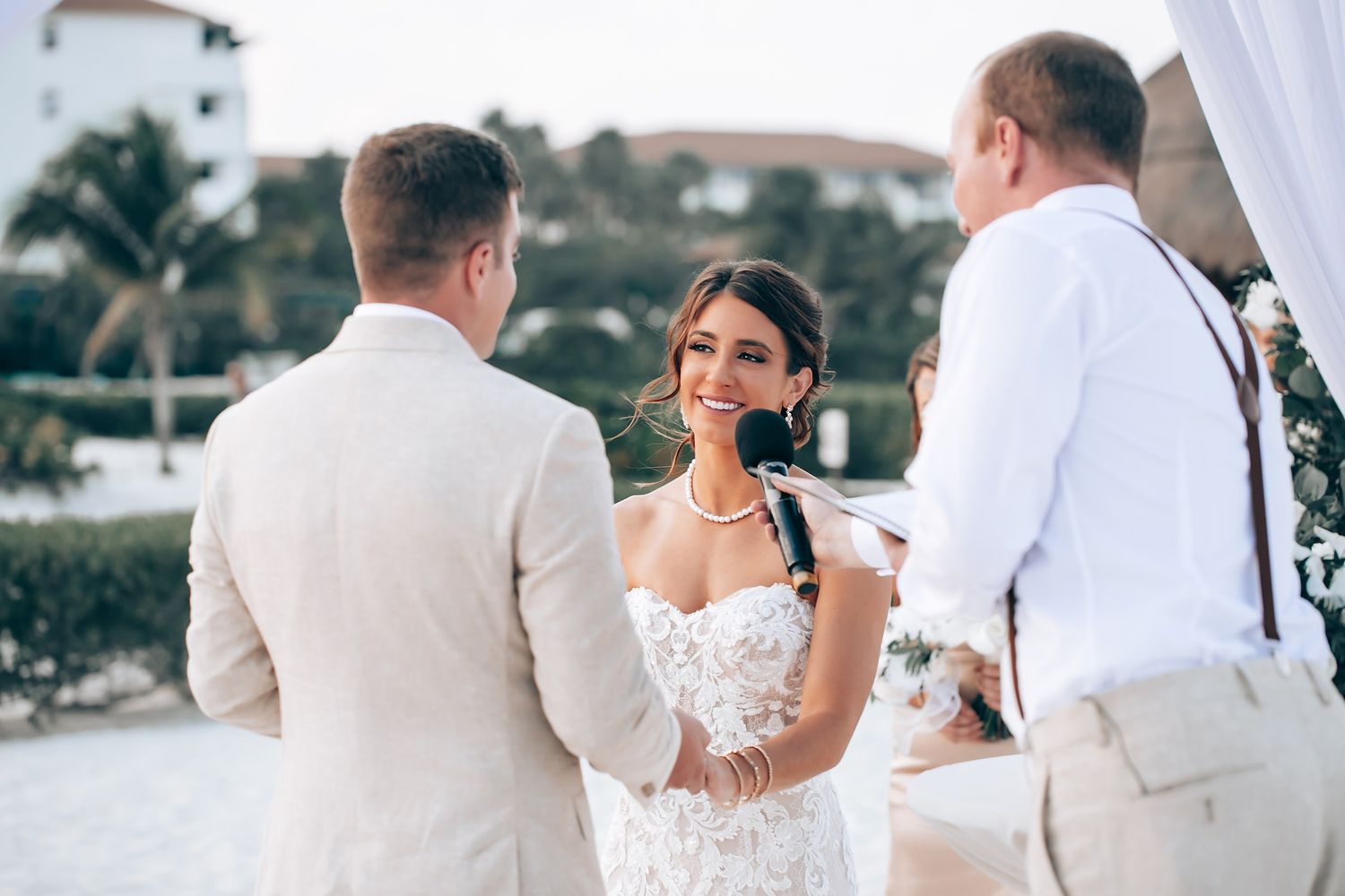 Elegant beachside wedding ceremony with white decor and guests in formal attire.