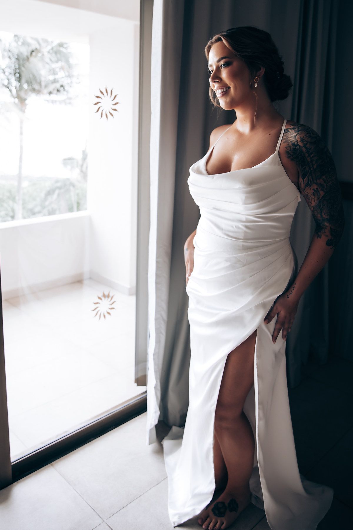 Person wrapped in white fabric poses artistically by a bright window.