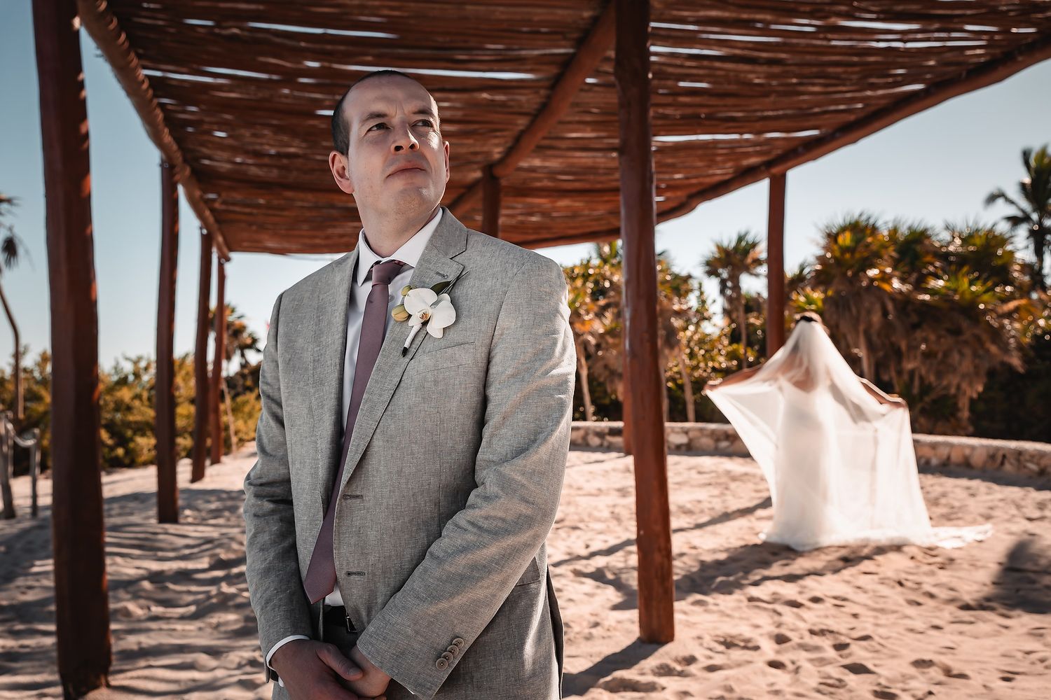 Wedding ceremony setup on a beach with wooden pergola and tropical landscaping.