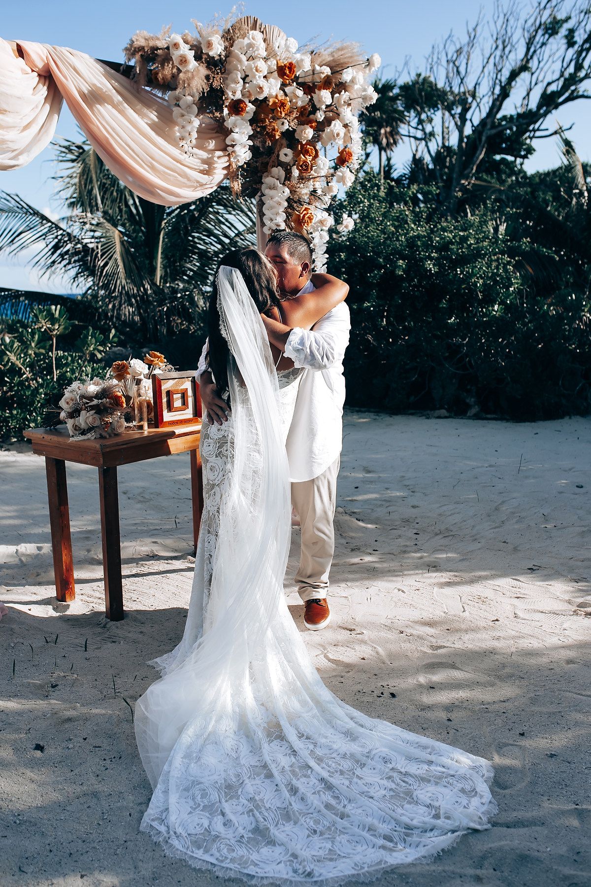 Elegant beach wedding ceremony setup with flowing white fabric and floral arrangements on a sandy shore.