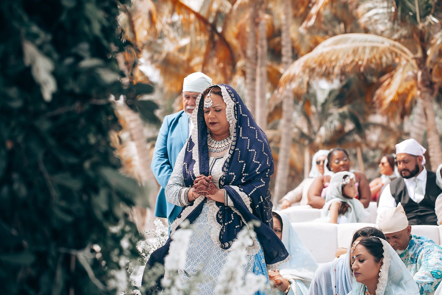 Wedding celebration on a beach with palm trees and traditional cultural attire.