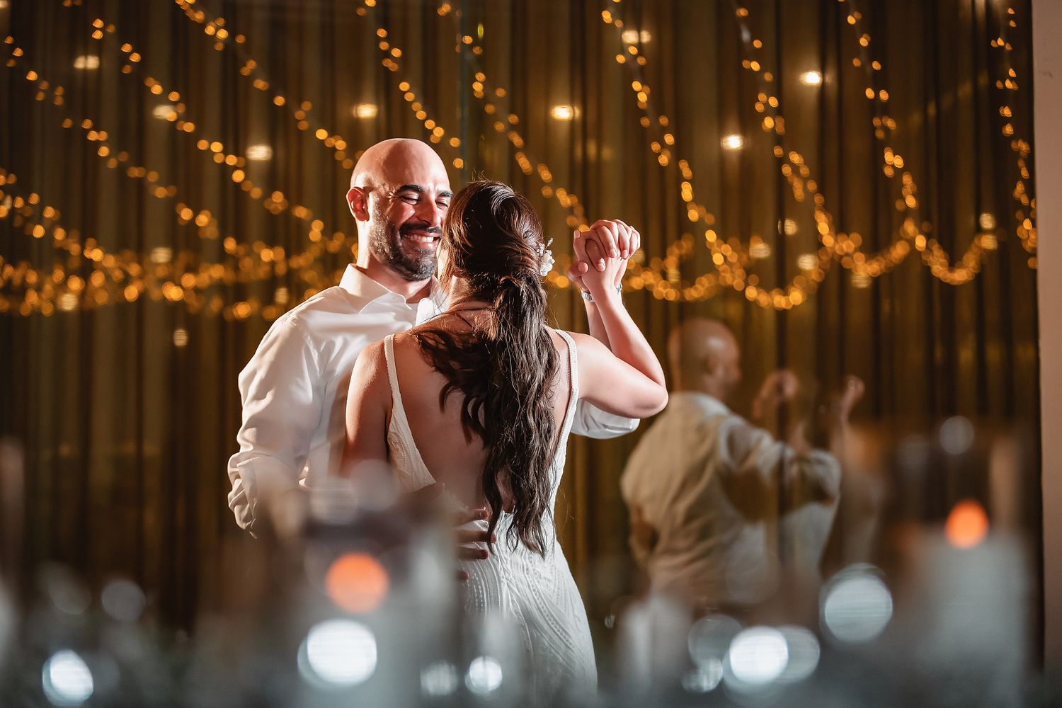 Romantic dance moment captured under warm string lights at wedding reception.