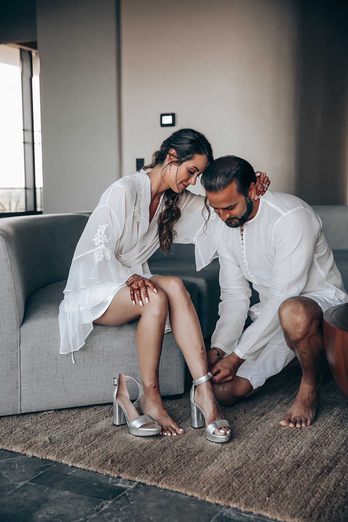 Couple sitting together on a brown carpet wearing white outfits in a minimalist indoor setting.