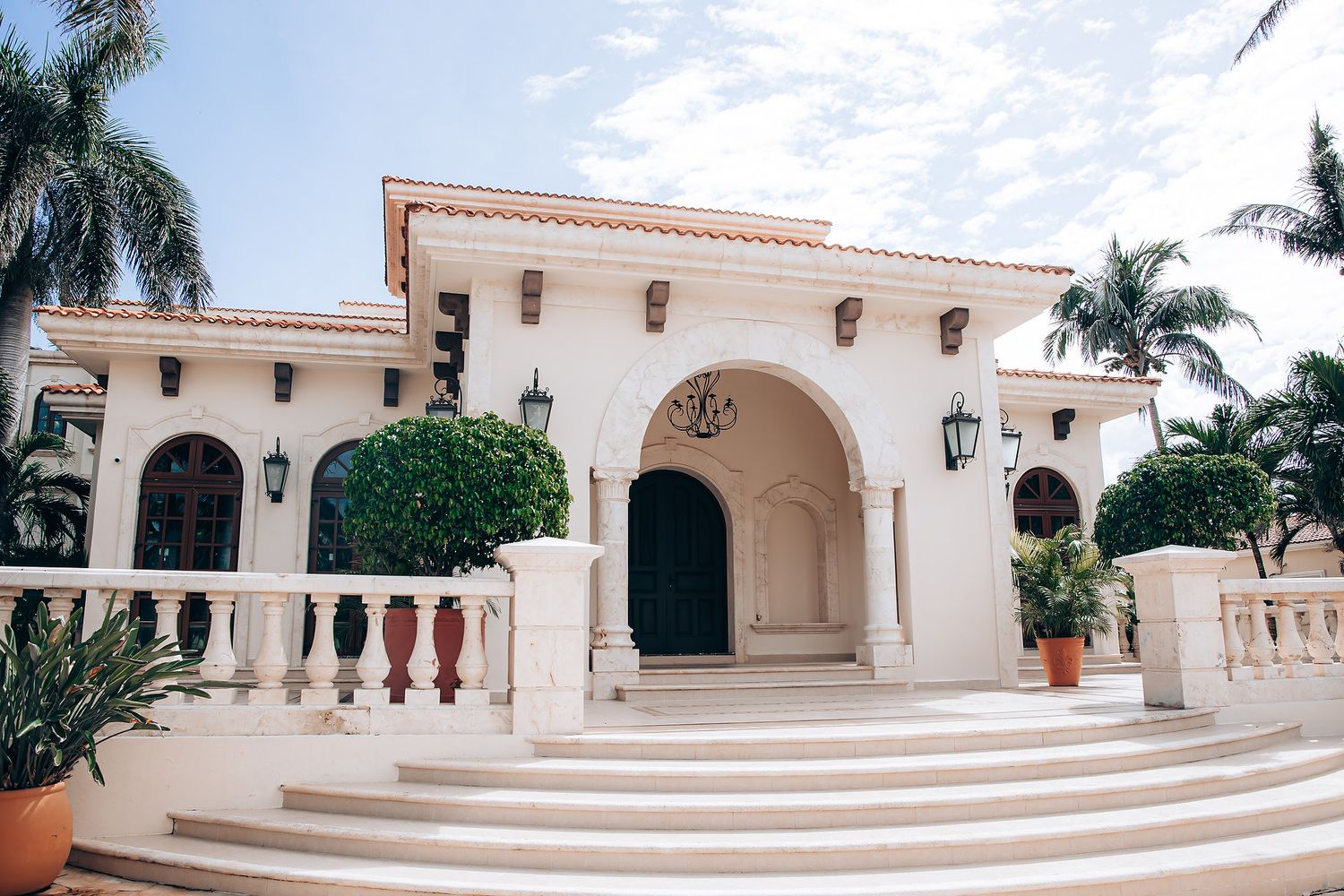 White Spanish colonial architecture with arched walkways and palm trees creates an elegant courtyard setting in tropical surroundings.