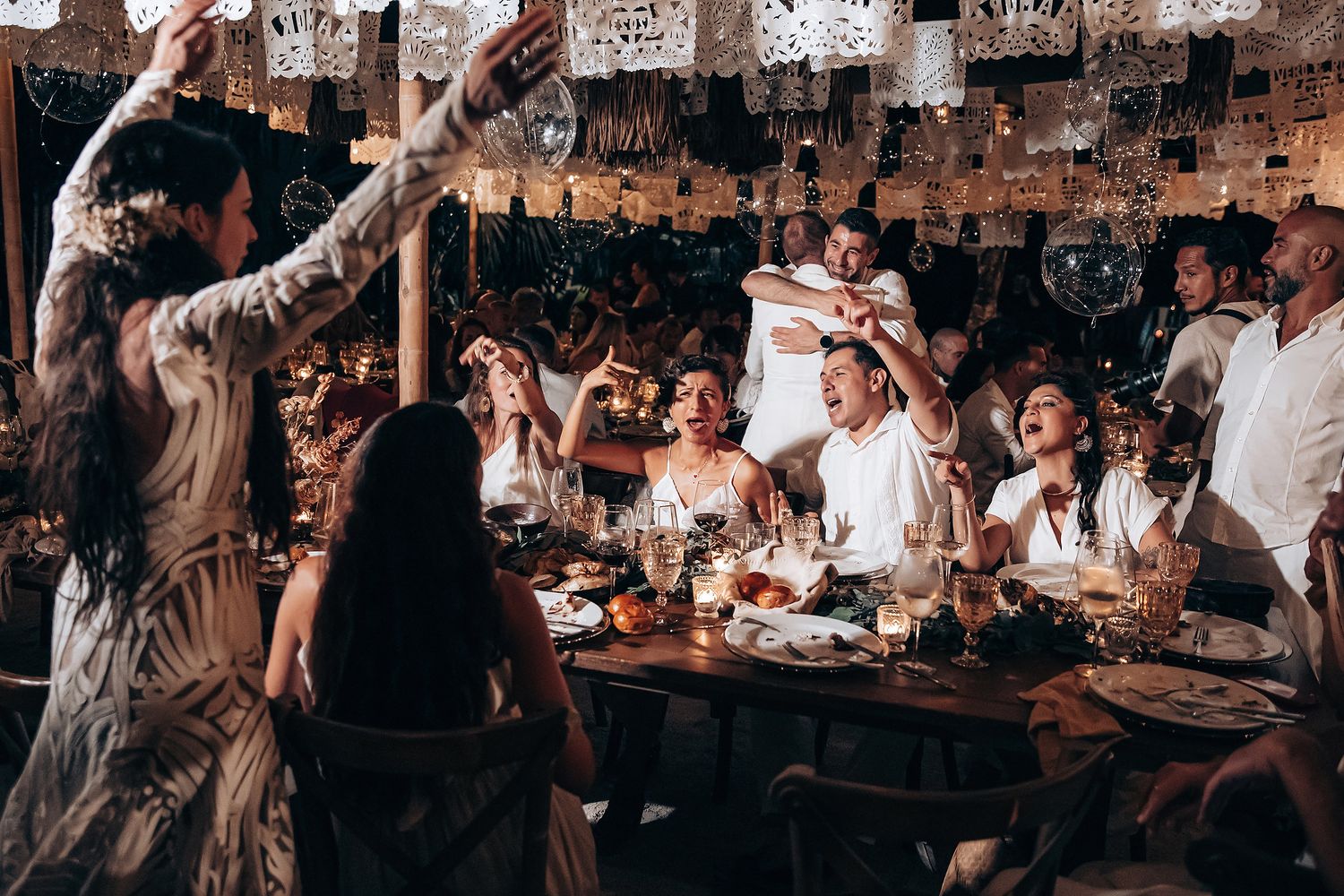 Guests seated at long tables during an outdoor wedding reception with string lights overhead.