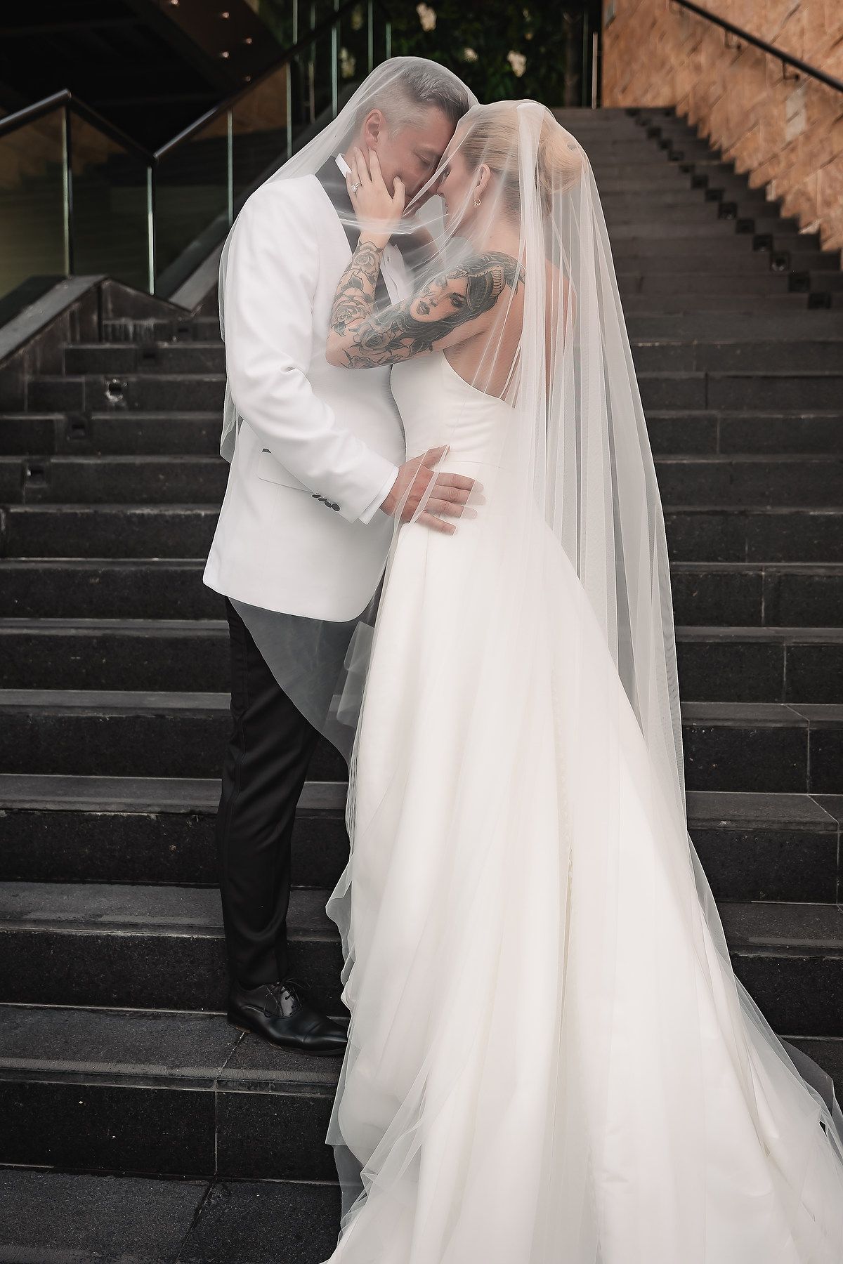 Romantic black and white wedding photo series showing couple embracing on stone steps with flowing white veil and dress.