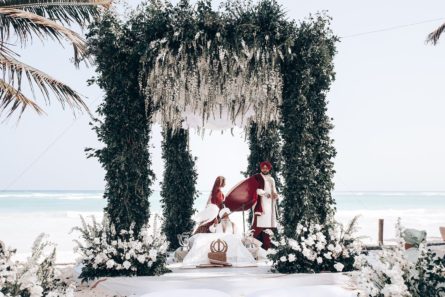 Floral arch and white decor create an elegant backdrop for a beachside wedding ceremony.