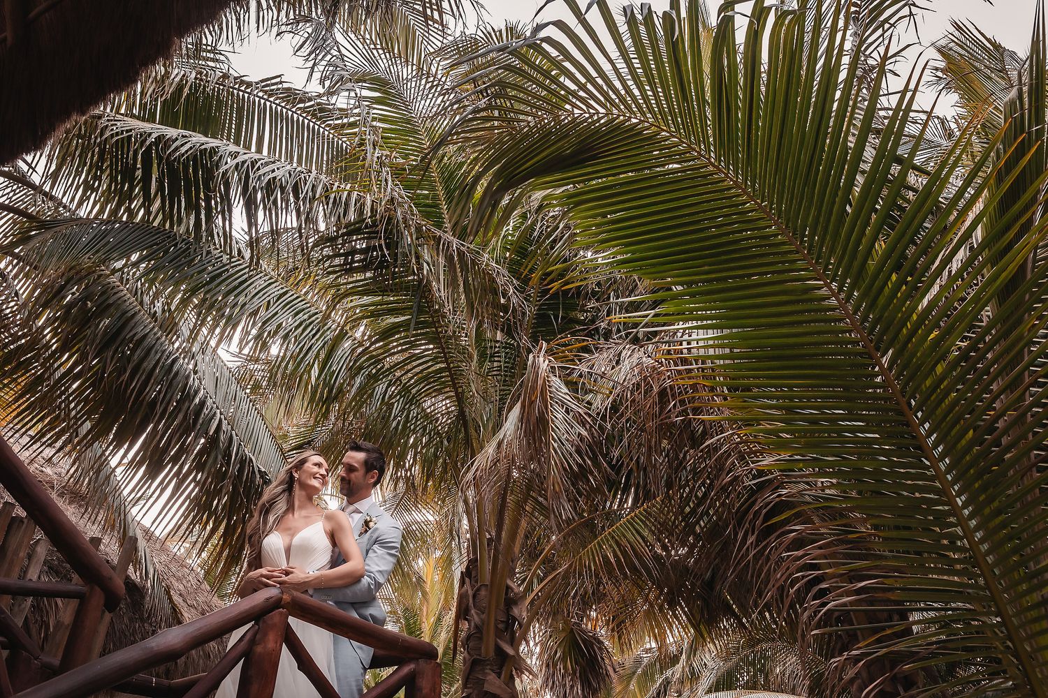 Palm fronds frame an intimate tropical beach wedding scene.