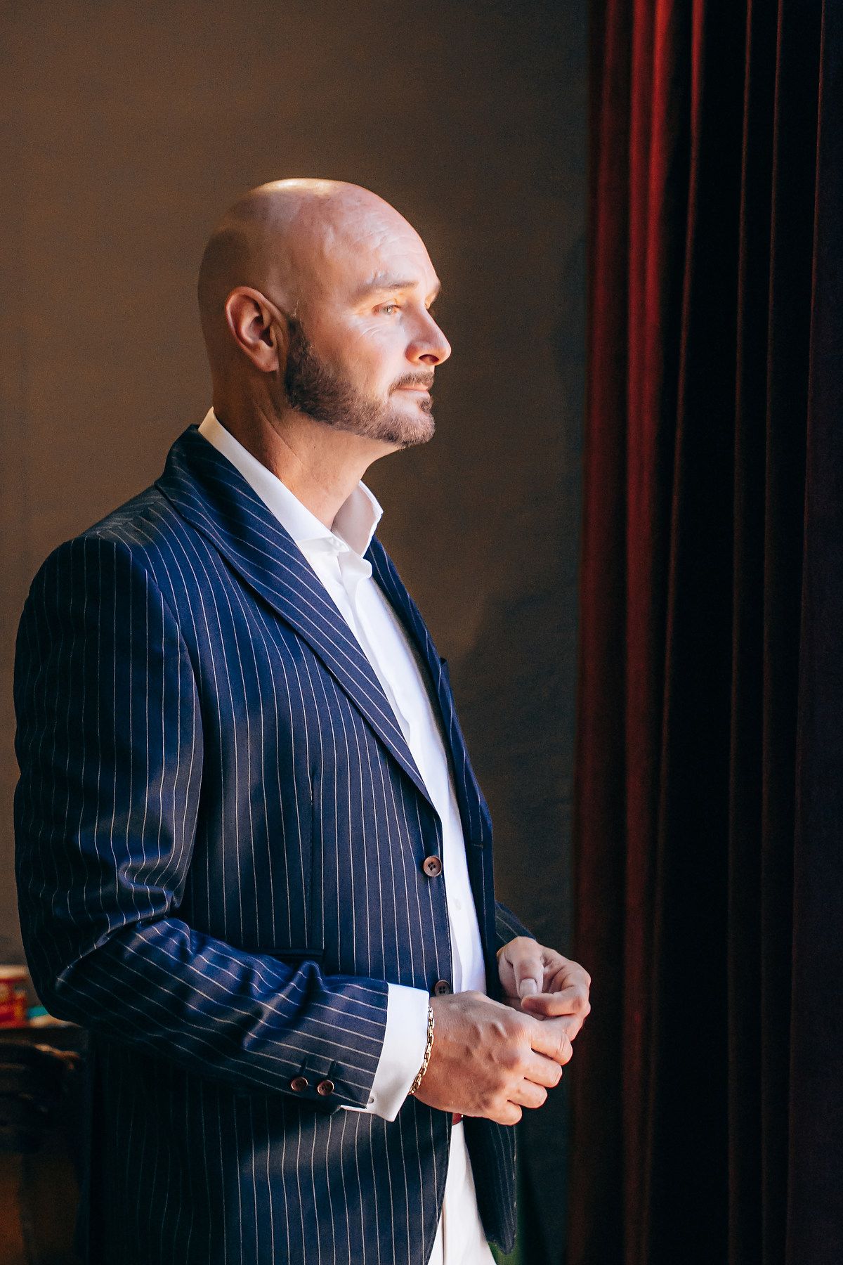 Professional wearing a navy pinstripe suit and white shirt stands in dramatic lighting against dark background.