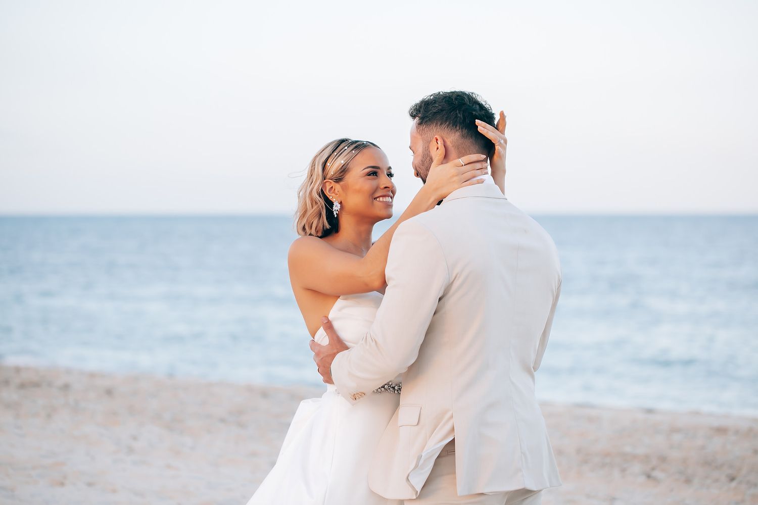 A couple shares a romantic embrace during their beach wedding with the ocean in the background.