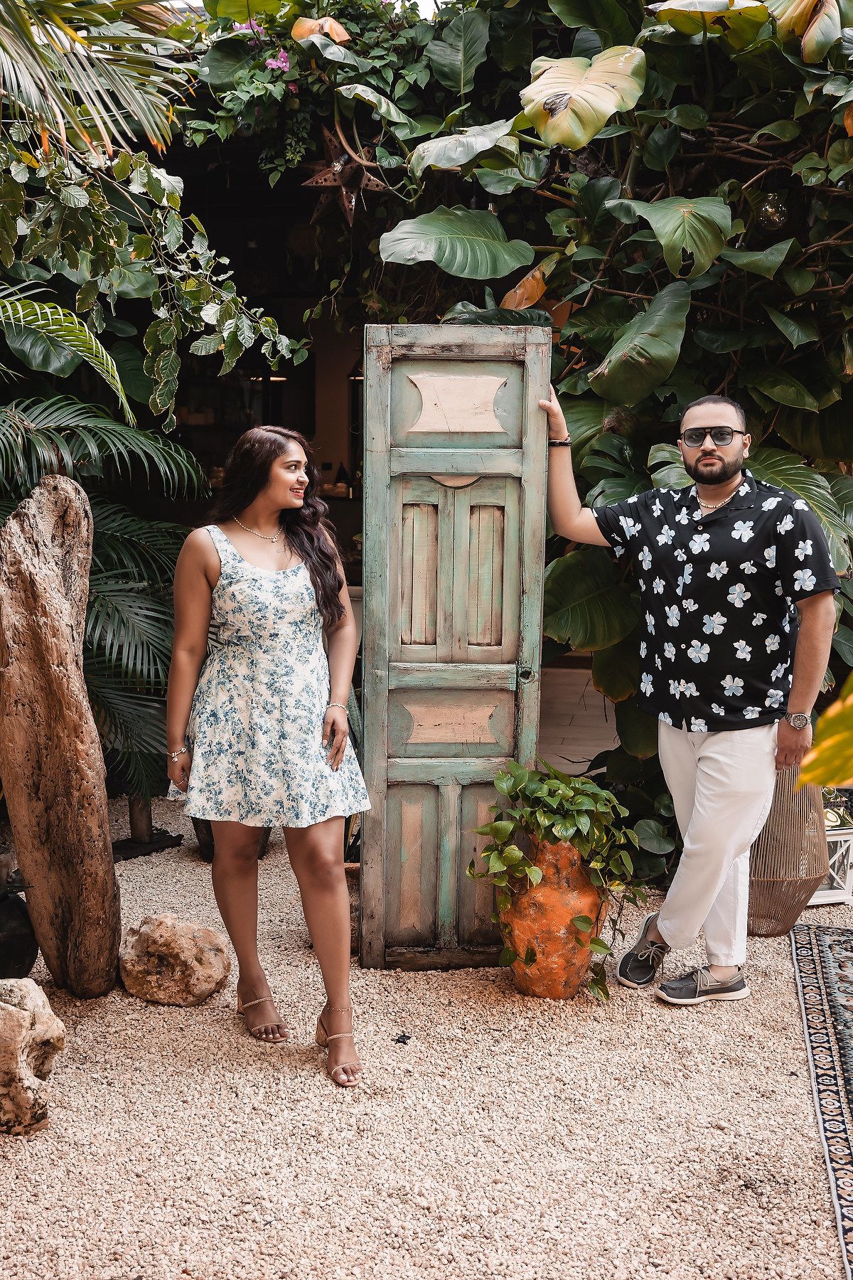 A couple's engagement moment captured against a vintage door in a tropical garden.