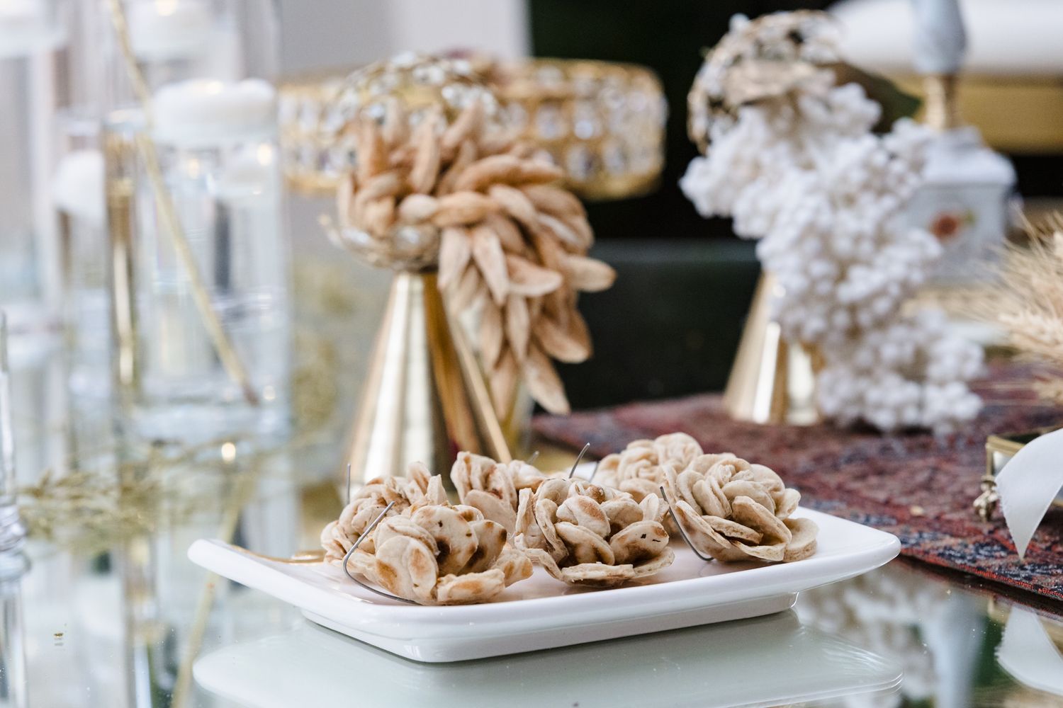 White plate of golden shell-shaped cookies on a glass table with elegant gold decorations and white floral arrangements.
