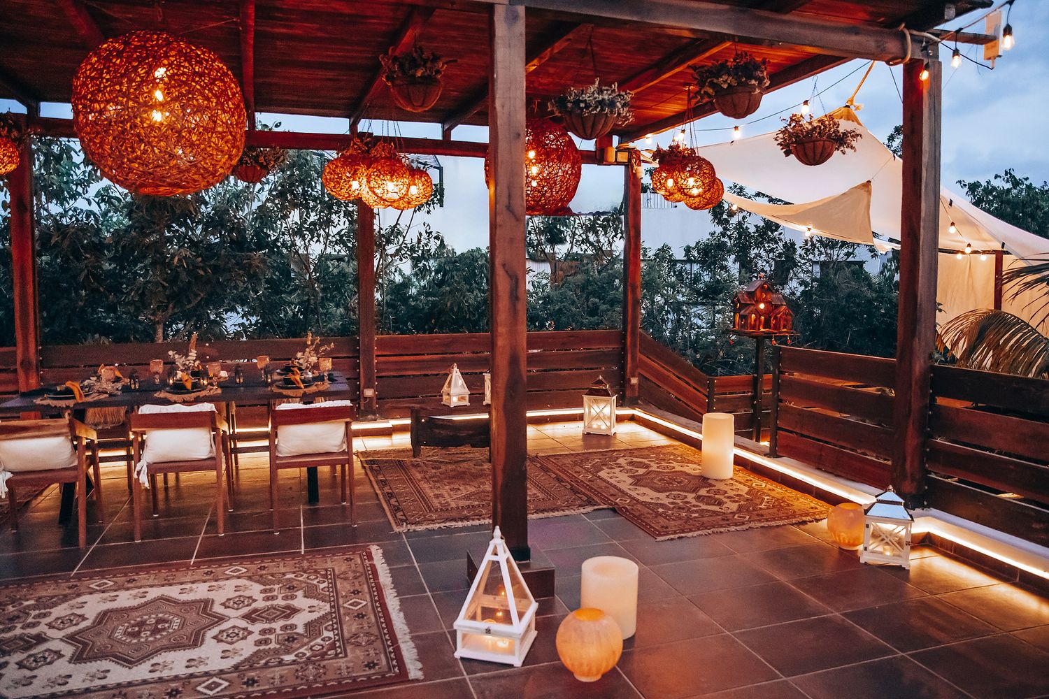 Boho outdoor wedding reception terrace with wicker pendant lights, candles, and rustic dining setup at dusk.
