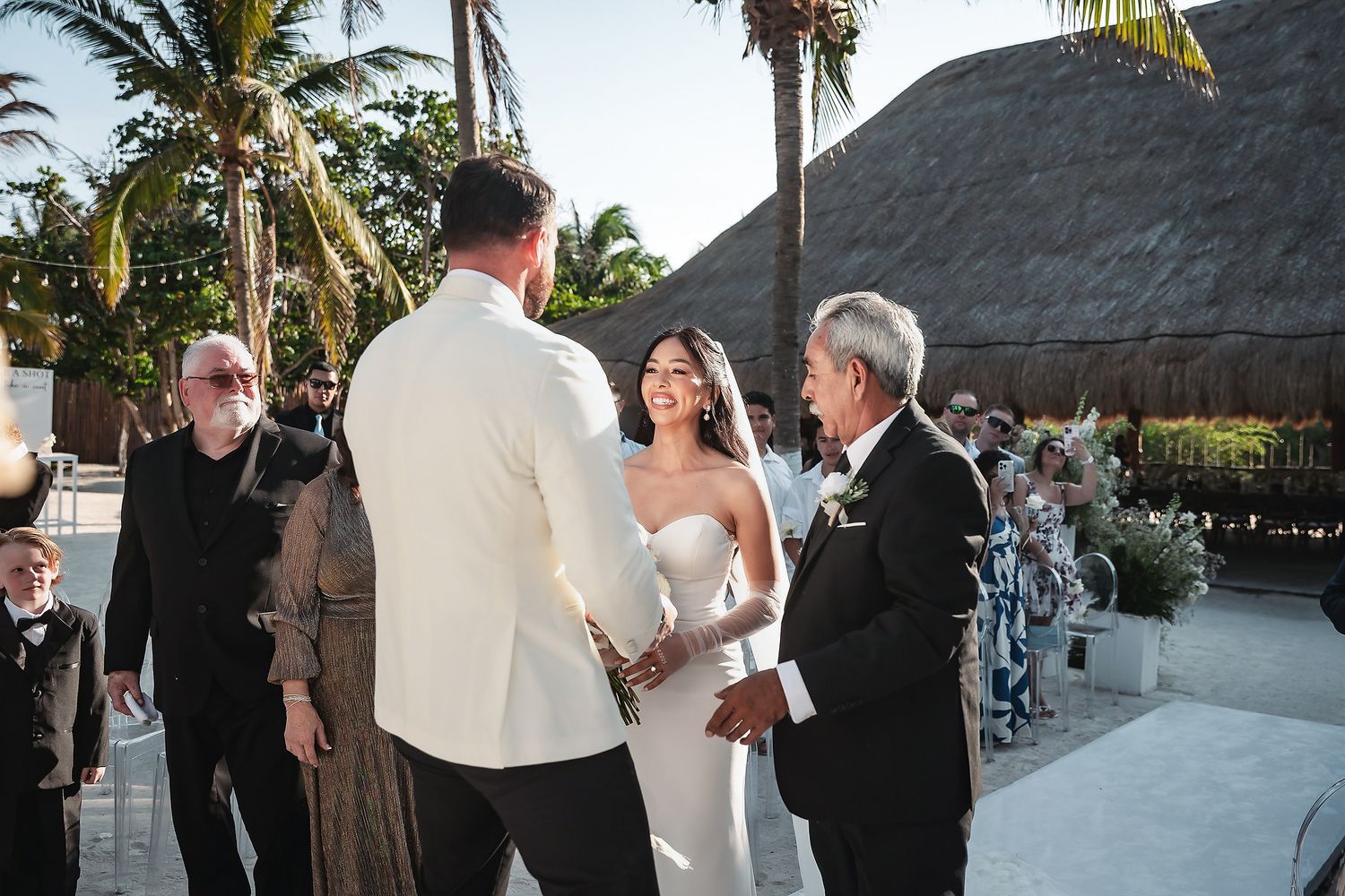 Bride and groom hold hands at altar with officiant during elegant outdoor beach wedding ceremony.