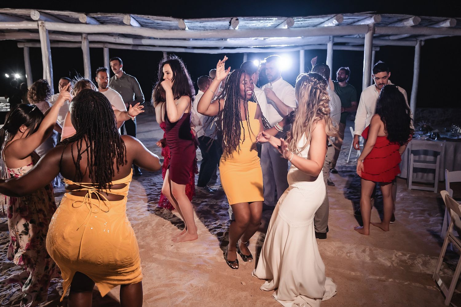 Wedding guests dance joyfully on sandy outdoor dance floor during evening beach wedding reception.