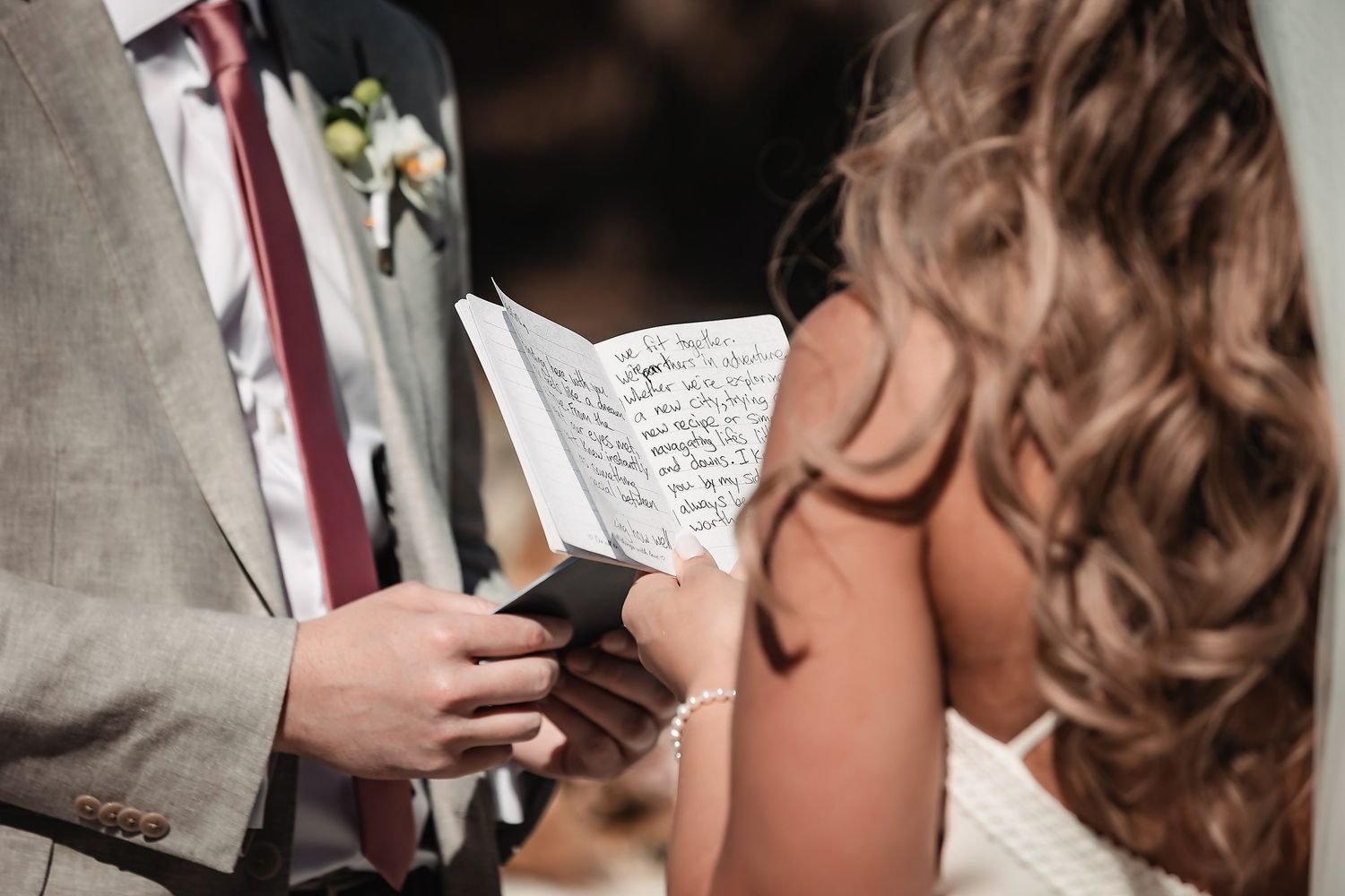 Groom reading heartfelt wedding vows from a small book during an intimate ceremony.