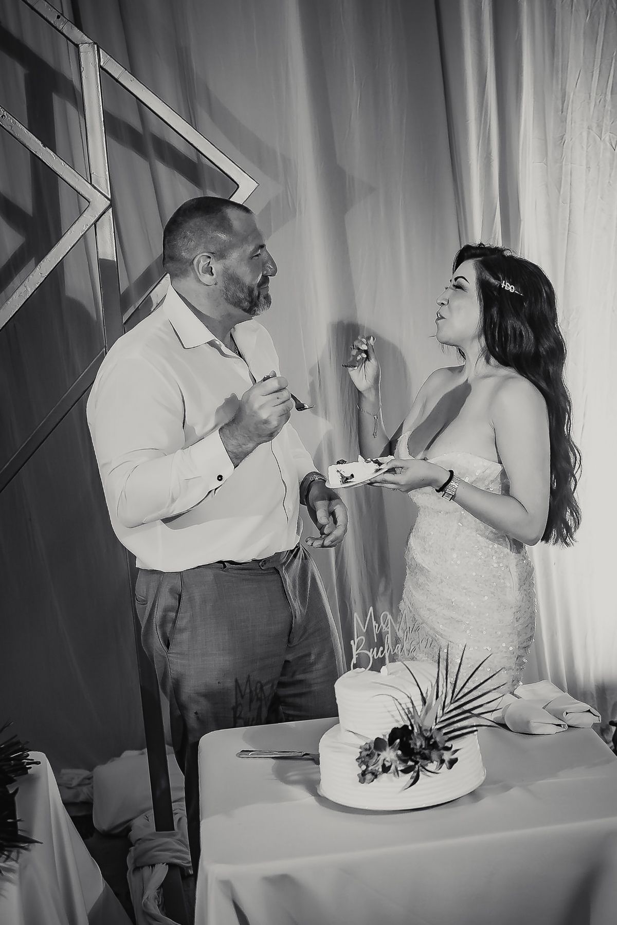 Black and white photo of bride and groom cutting wedding cake at elegant reception ceremony.