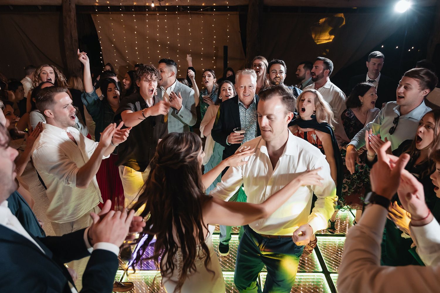 Excited wedding guests dance and celebrate together on a illuminated dance floor at a festive reception.