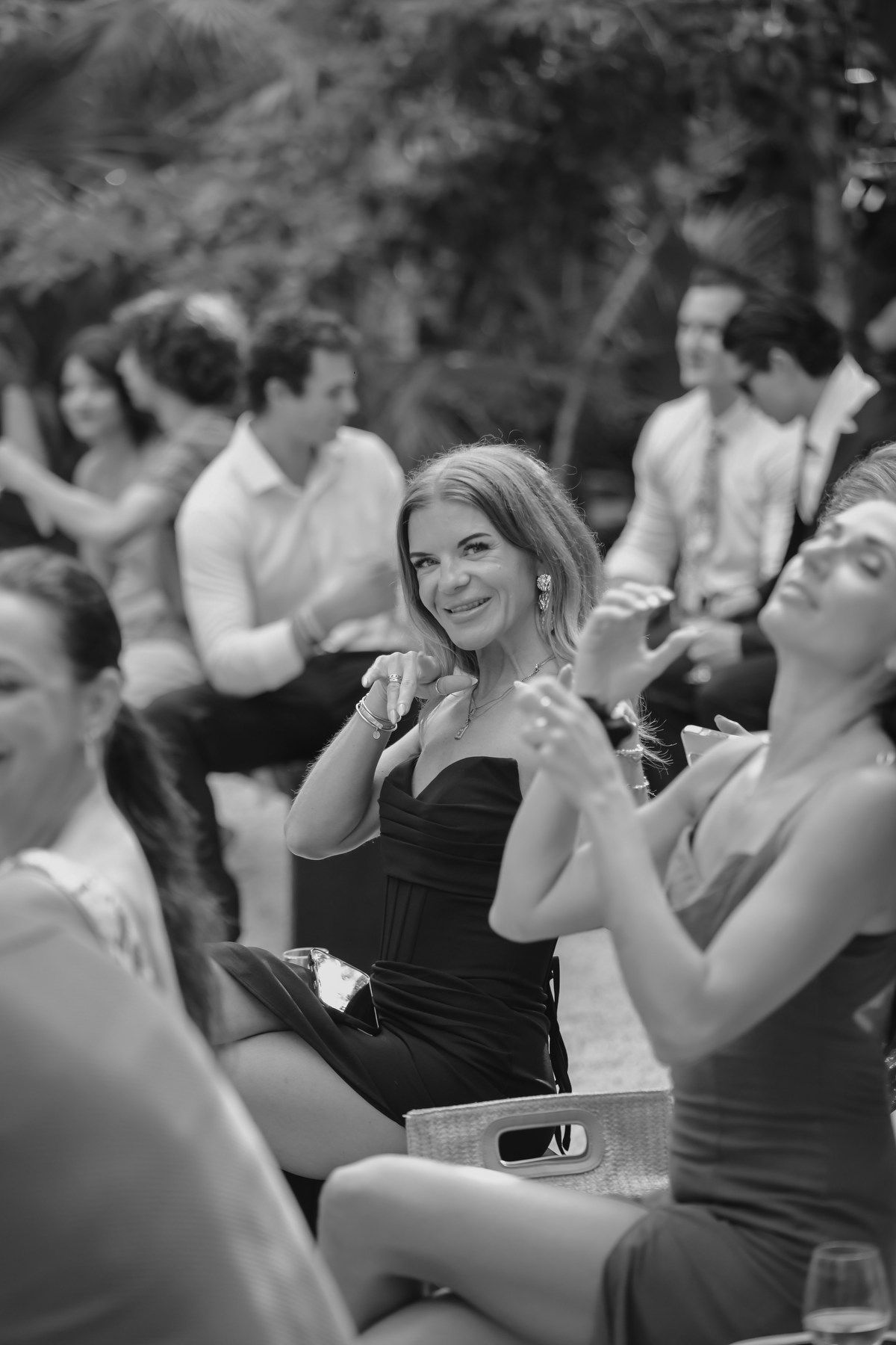Smiling woman in black dress clapping at outdoor wedding reception, black and white photo.