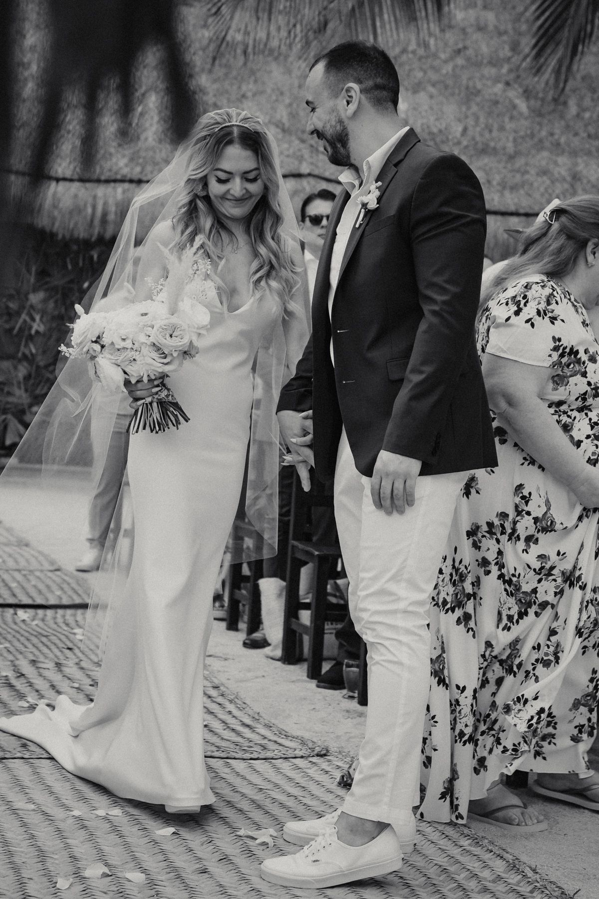 Black and white photo of bride and groom walking down the aisle at an outdoor beach wedding ceremony.
