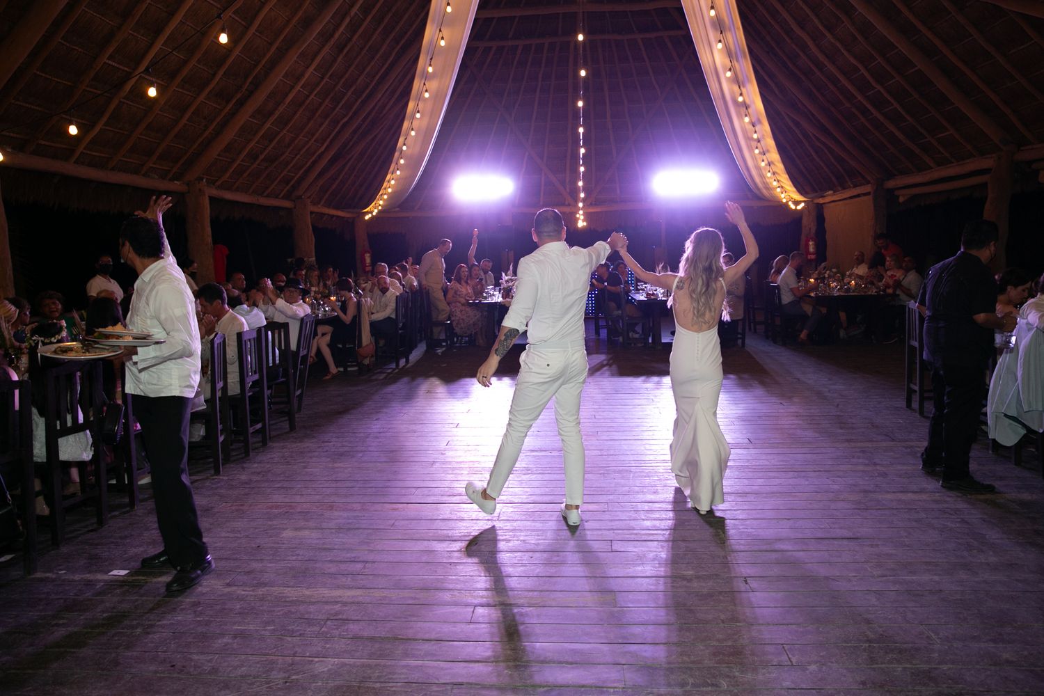 Bride and groom make grand entrance onto dance floor in warmly lit rustic wedding reception venue.