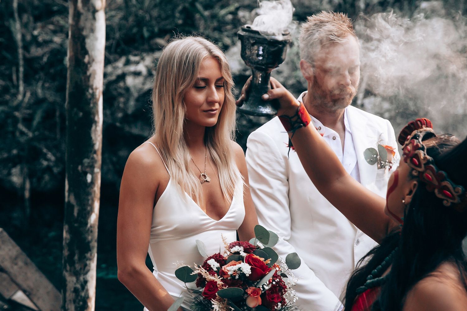 Wedding ceremony participants gather on a wooden deck surrounded by trees and natural scenery.