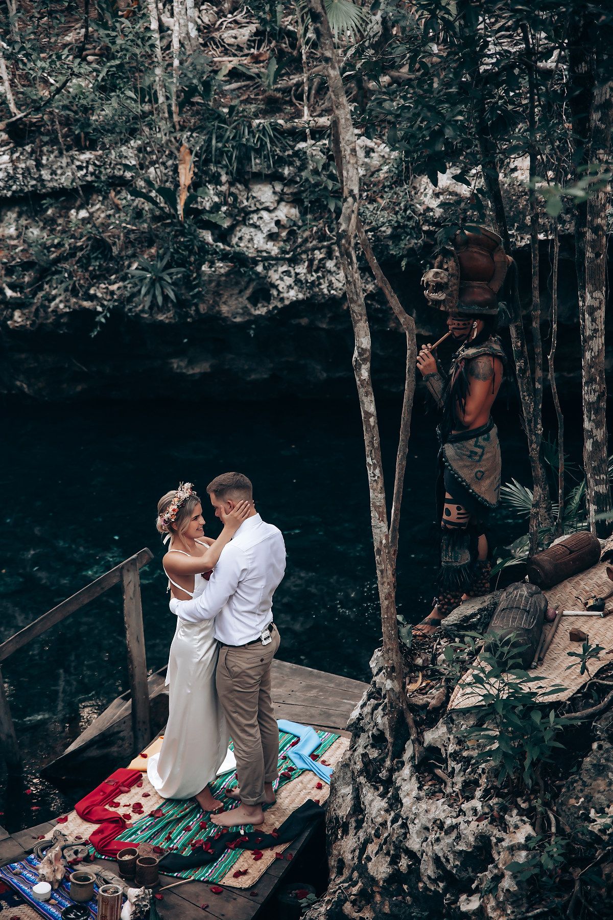 A couple shares a tender moment on a blanket in a scenic forest cave setting.