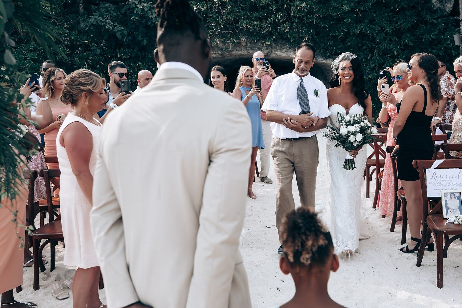 Outdoor wedding ceremony with guests seated on wooden chairs surrounded by greenery.