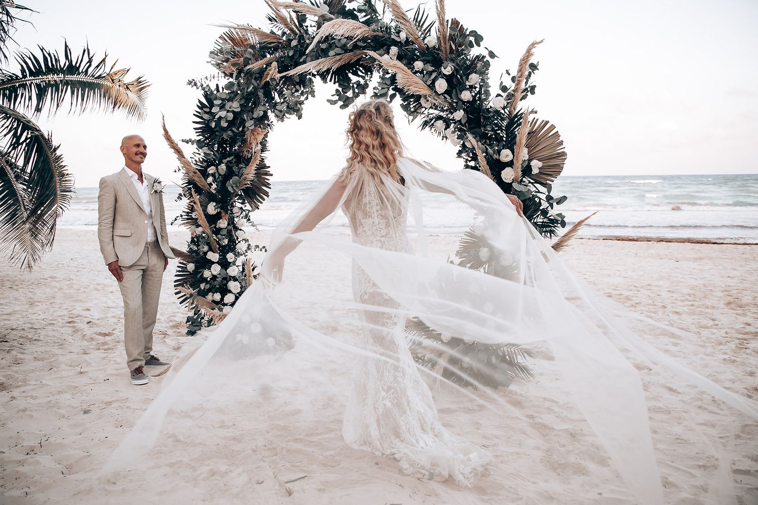 Flowing white wedding dress billowing in beach breeze during photoshoot.