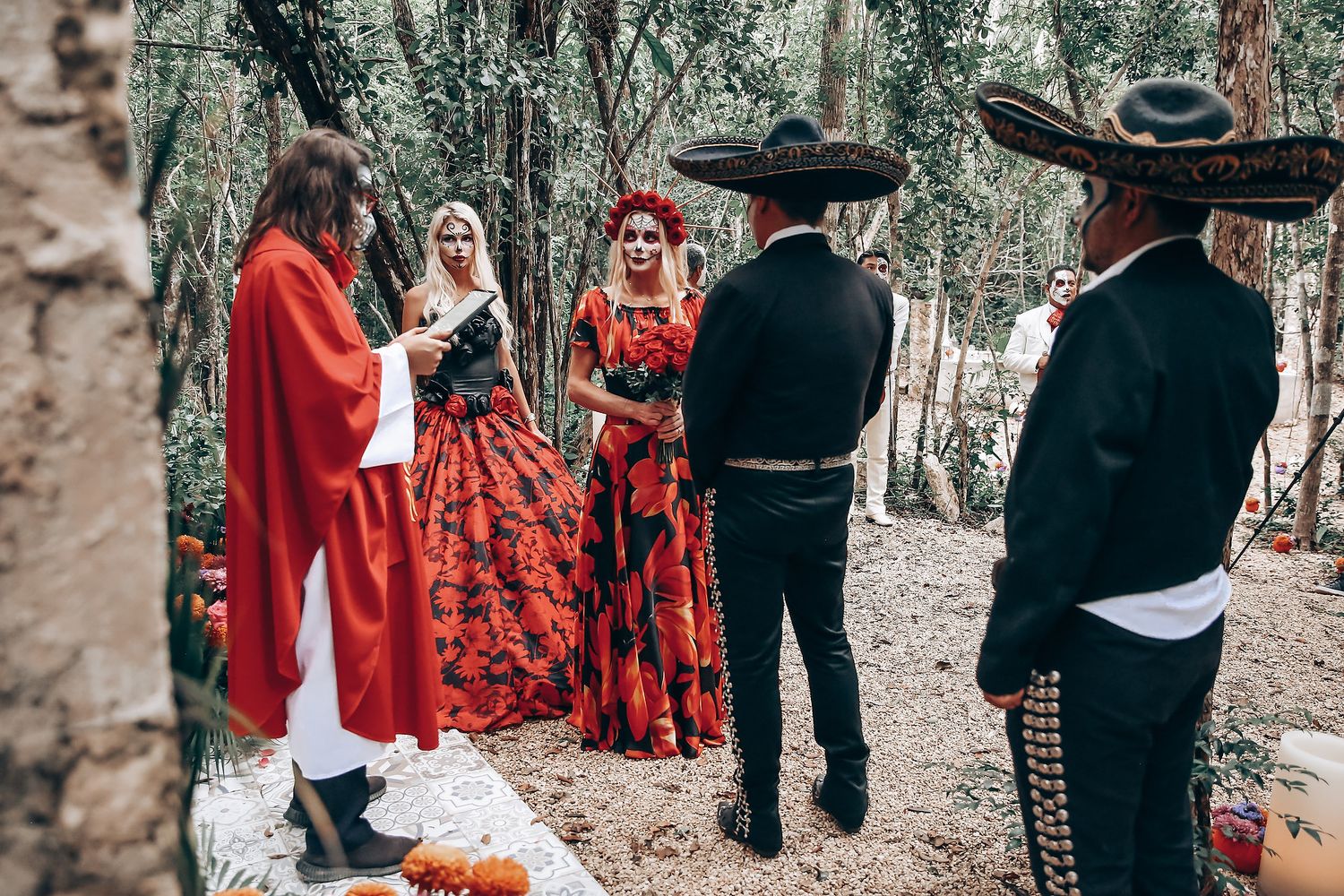 Gothic wedding scene with figures in red dresses and black attire gathered in outdoor woodland setting.