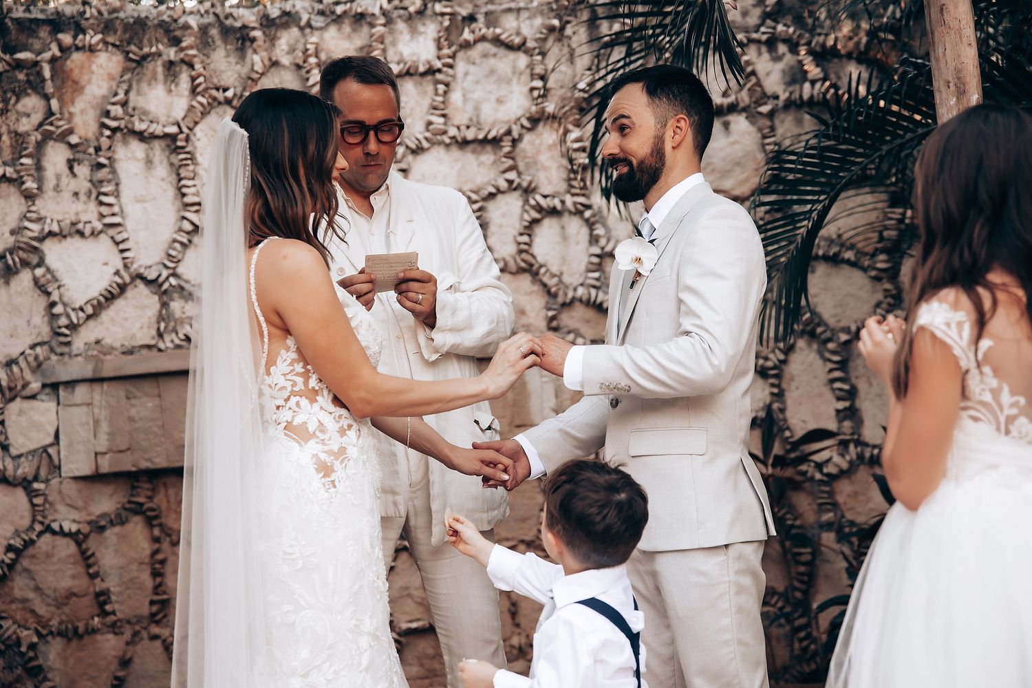 Intimate wedding ceremony moment against stone wall backdrop with floral decorations.