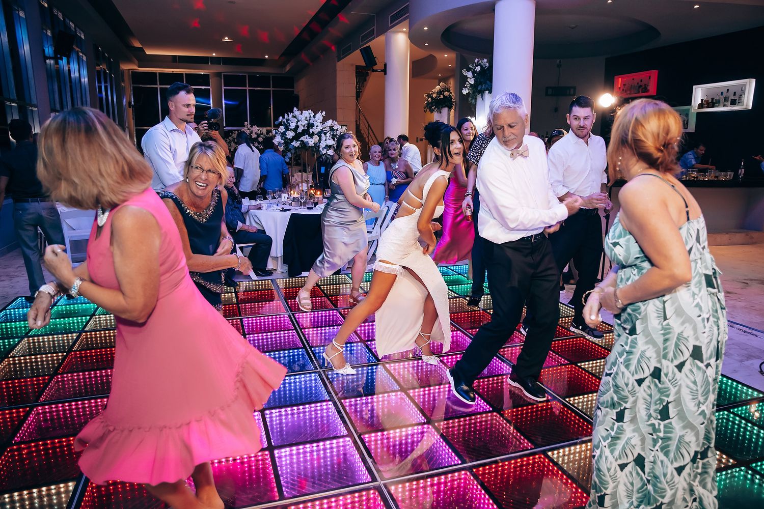 Colorful LED dance floor illuminated at wedding reception with guests dancing.