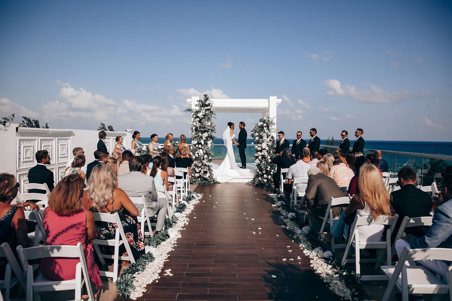 Outdoor wedding ceremony setup with white chairs and aisle runner facing the ocean view.