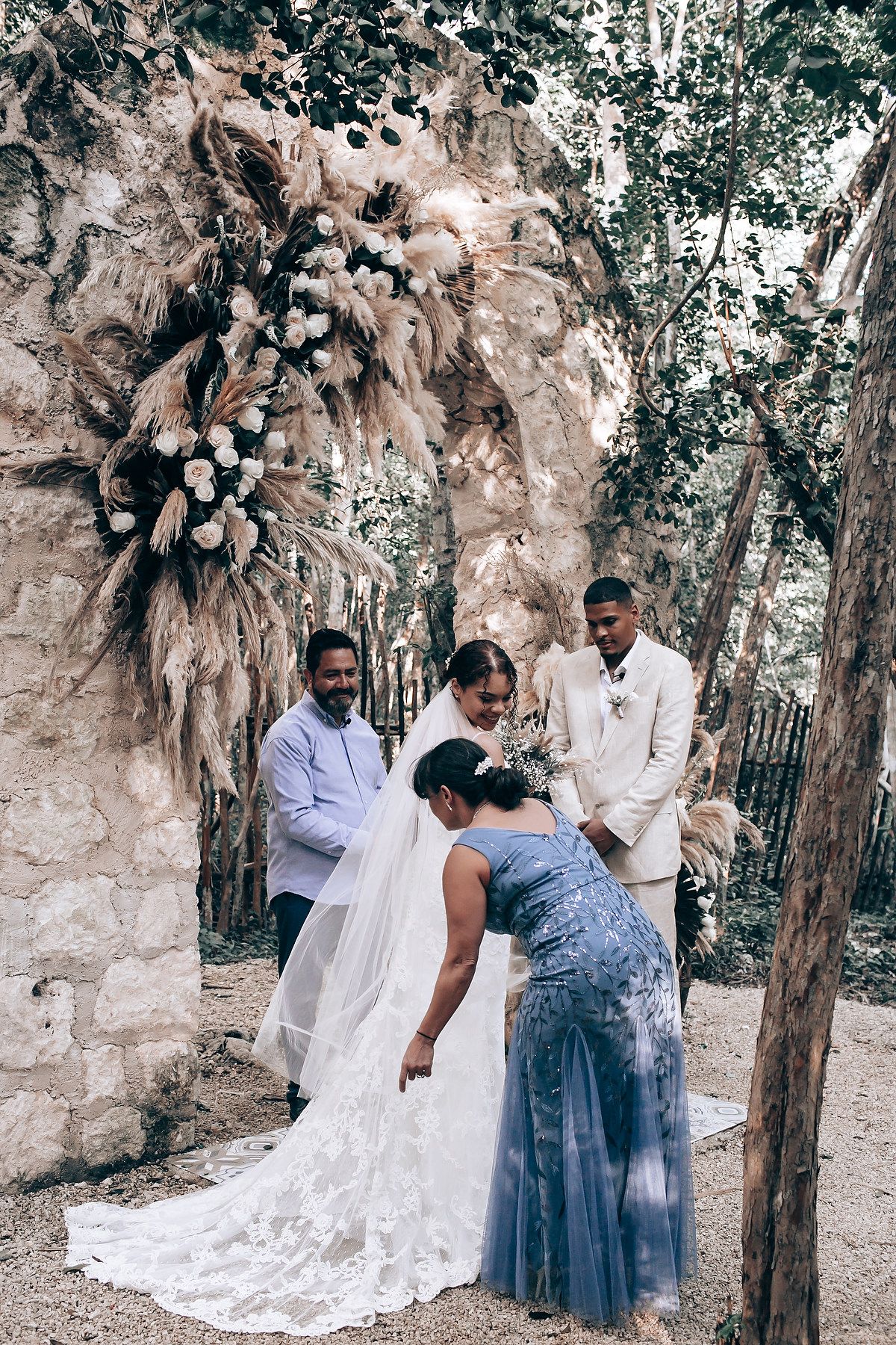 A wedding party gathers in a wooded area with stone walls and natural decor.