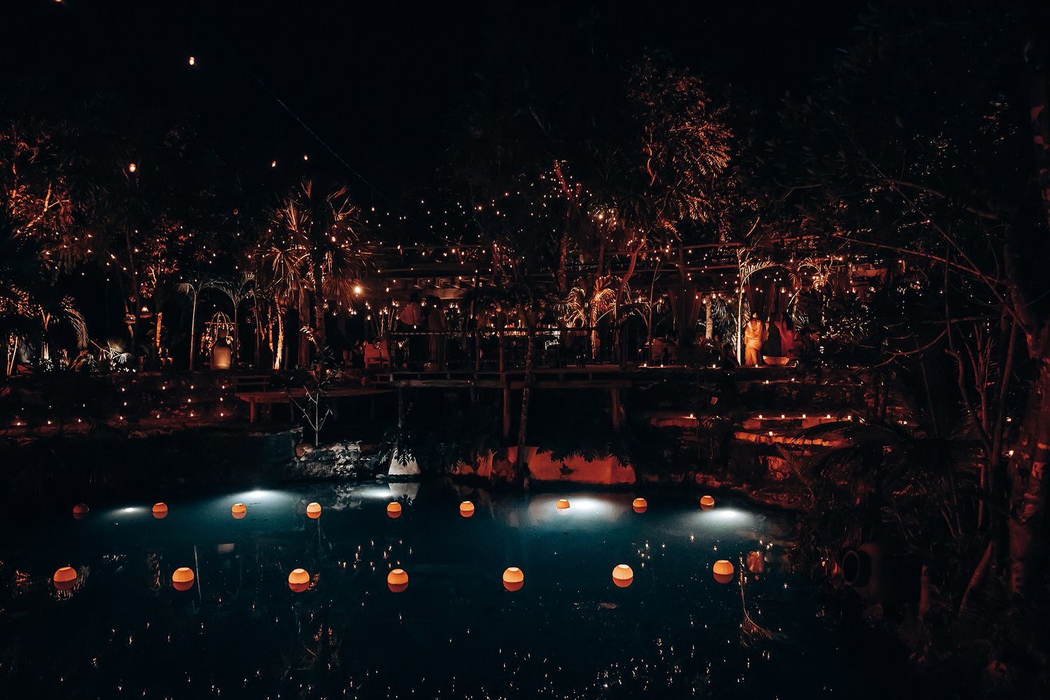 Wedding guests dance and celebrate on an outdoor dance floor illuminated by warm string lights at night.